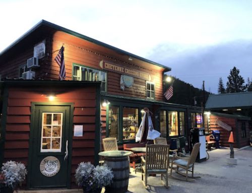 A rustic wooden building with a sign reading "Cheyenne Crossing" and outdoor seating, illuminated at dusk.