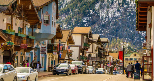 Charming street lined with colorful buildings, shops, and cars, set against a backdrop of snow-capped mountains.