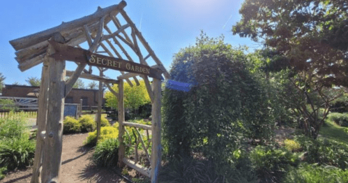 A wooden archway labeled "Secret Garden" leads into a lush, green garden area under a bright blue sky.