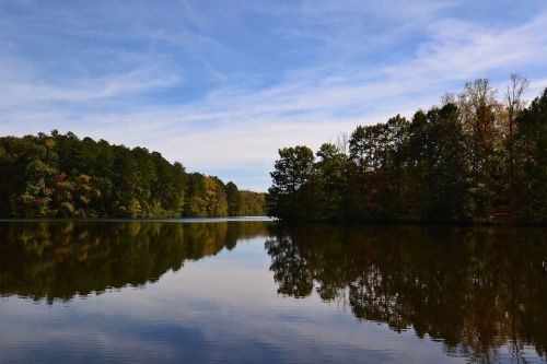 A serene lake surrounded by trees, reflecting the blue sky and autumn foliage.