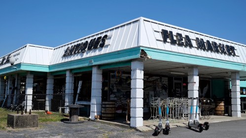 A bright blue and white building with a sign reading "Flea Market," featuring outdoor displays and scooters parked outside.