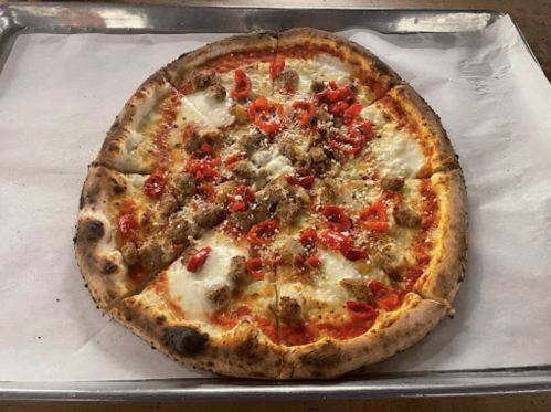 A freshly baked pizza topped with sausage, red peppers, and melted cheese on a parchment-lined tray.
