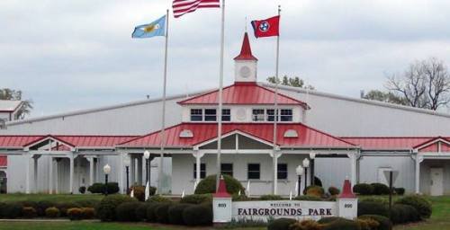 A white building with a red roof, flags flying, and a sign reading "Welcome to Fairgrounds Park."