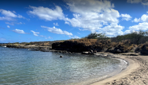 A serene beach scene with gentle waves, sandy shore, and a clear blue sky dotted with clouds.