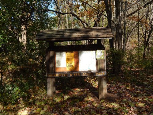 Information sign at Quinnipiac River State Park surrounded by autumn foliage and trees.