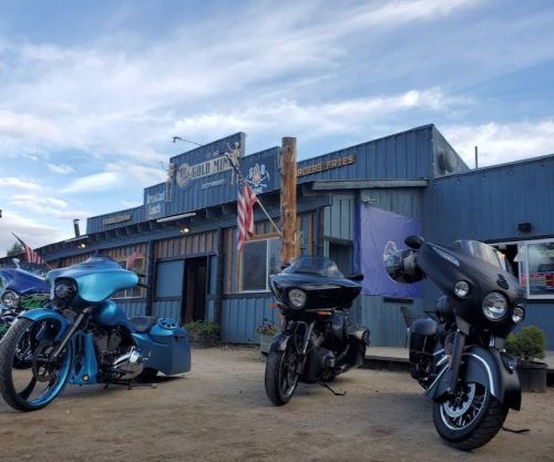 Three motorcycles parked in front of a blue building with flags, under a cloudy sky.