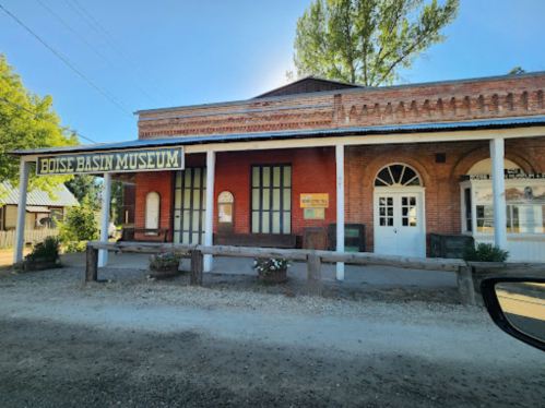 Exterior of the Boise Basin Museum, featuring brick architecture and a sign, surrounded by trees and gravel road.