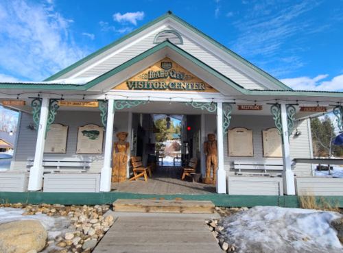 Idaho City Visitor Center with wooden sculptures, benches, and a clear blue sky in the background. Snow on the ground.