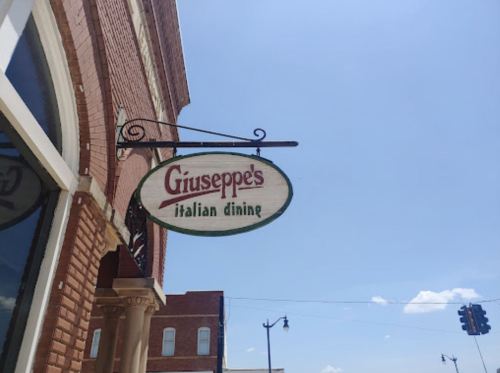 Sign for Giuseppe's Italian dining hanging from a brick building under a clear blue sky.