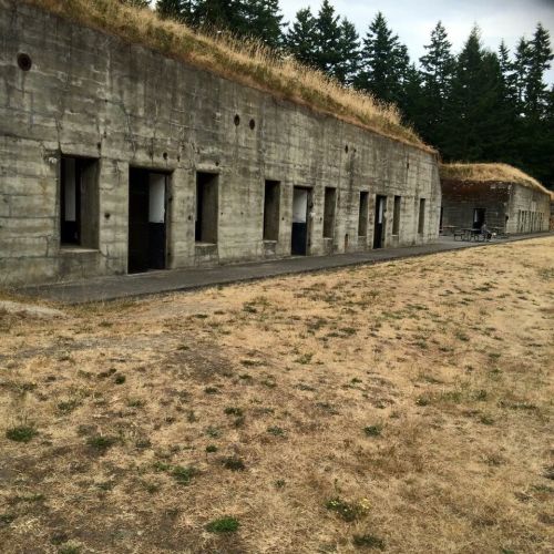 A concrete building with multiple doorways, surrounded by dry grass and trees in the background.