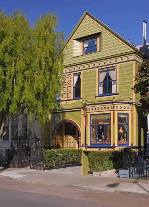 Colorful Victorian house with green siding, decorative trim, and large windows, surrounded by lush greenery.