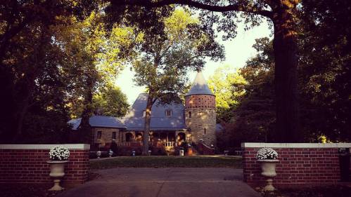 A picturesque stone castle surrounded by lush trees, with a tower and a welcoming entrance.