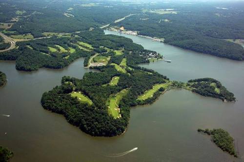 Aerial view of a lush, green island surrounded by water, featuring golf courses and wooded areas.