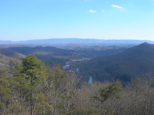 A panoramic view of rolling mountains and a winding river under a clear blue sky.
