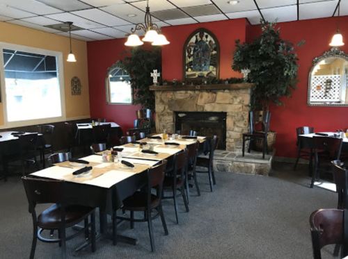 Cozy restaurant interior with a stone fireplace, tables set for dining, and warm red and yellow walls.