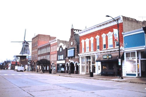 A quiet street lined with historic buildings, featuring a windmill in the background and shops along the sidewalk.