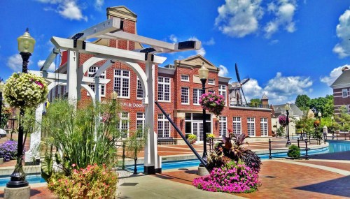 A vibrant outdoor scene featuring a brick building, colorful flowers, and a clear blue sky with fluffy clouds.
