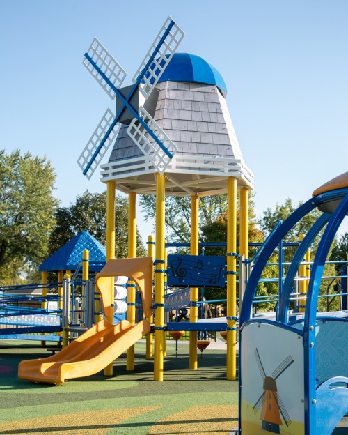 Colorful playground featuring a windmill structure, slide, and various play areas under a clear blue sky.