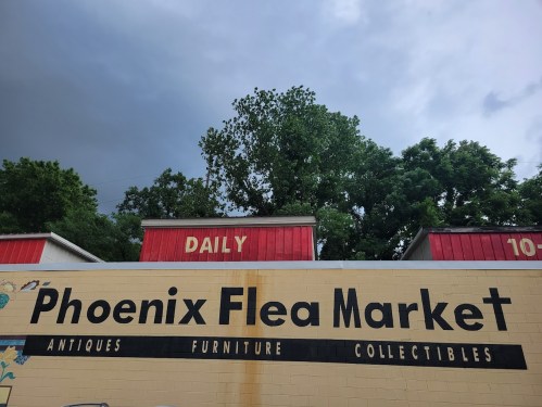 Sign for Phoenix Flea Market featuring "Antiques, Furniture, Collectibles" under a cloudy sky.