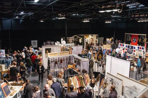A bustling indoor market with various vendor booths and a crowd of people browsing and shopping.
