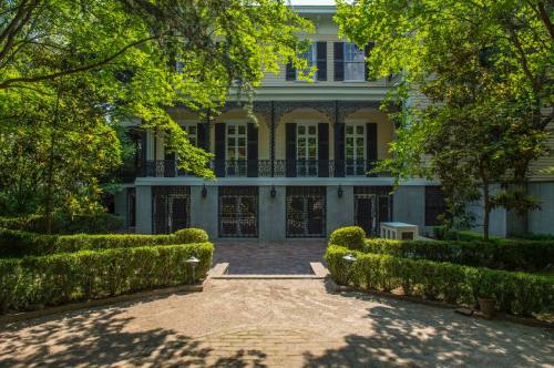 A charming two-story house surrounded by lush greenery and neatly trimmed hedges, featuring a welcoming entrance.