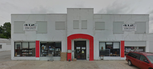 A storefront with a red arch entrance, large windows displaying items, and a red car parked outside.