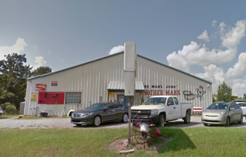 A large metal building with signs reading "One Man's Junk" and "Another Man's Treasure," surrounded by parked cars.
