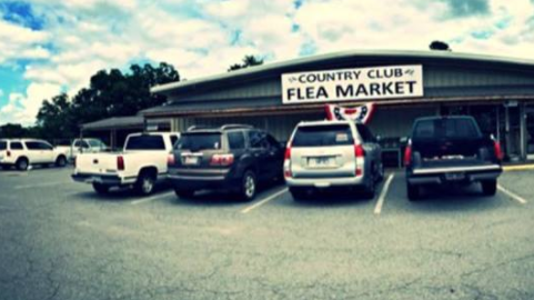 Exterior of the Country Club Flea Market with parked cars and a cloudy sky in the background.