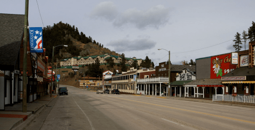 A quiet street in a small town with historic buildings and a hillside hotel in the background under a cloudy sky.
