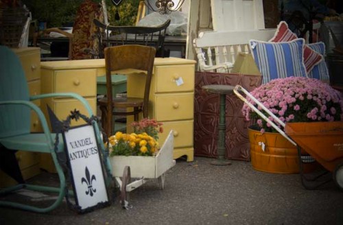 A collection of vintage furniture and decor items, including a yellow dresser, chairs, and potted flowers.