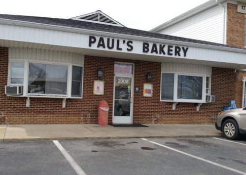 Exterior of Paul's Bakery with a red "OPEN" sign, brick facade, and parked car in front.