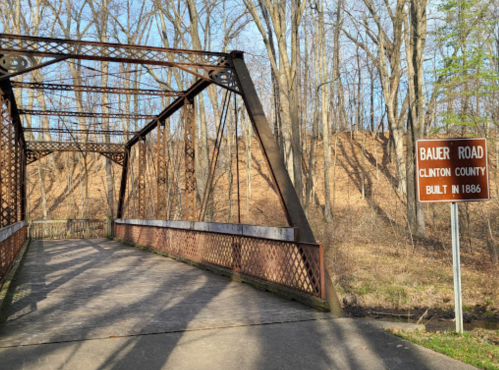 Historic Bauer Road bridge in Clinton County, built in 1886, surrounded by trees and a dirt hillside.