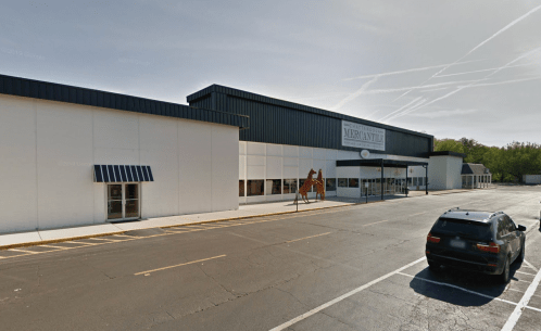 Exterior view of a large commercial building with a sign, parking lot, and a vehicle parked nearby.