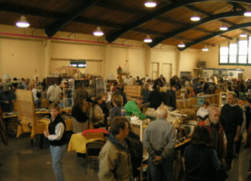 A bustling indoor market with numerous stalls and a crowd of people browsing various items.