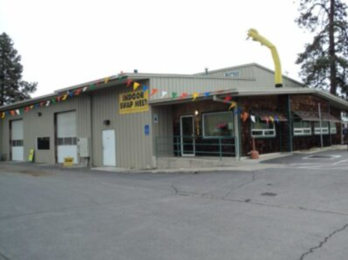A large metal building with colorful flags and an inflatable waving arm, labeled "Indoor Swap Meet."