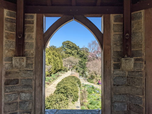 View through an arched doorway, framing a lush garden with trees and pathways under a clear blue sky.
