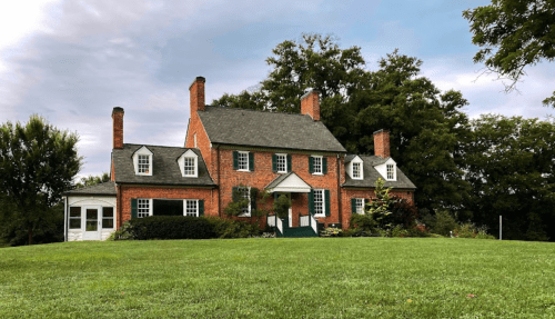 A charming brick house with a green lawn, surrounded by trees under a cloudy sky.