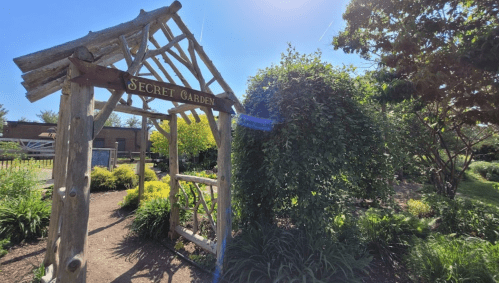 A wooden archway labeled "Secret Garden" leads into a lush, green garden under a bright blue sky.