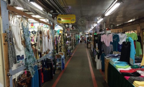 A bustling market aisle lined with colorful clothing displays and shoppers exploring various stalls.