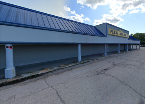 Exterior of a flea market building with a blue roof and a large sign, set against a cloudy sky.