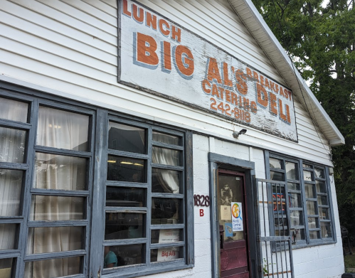 Exterior of Big Al's Deli, featuring a sign for lunch and breakfast, with large windows and a white building.