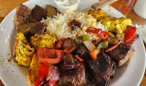 A plate of grilled meats, colorful peppers, and rice, accompanied by a small bowl of sauce.