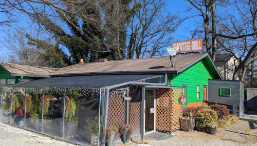 A green building with a sign reading "Frontier Grill," featuring a covered outdoor area and trees in the background.