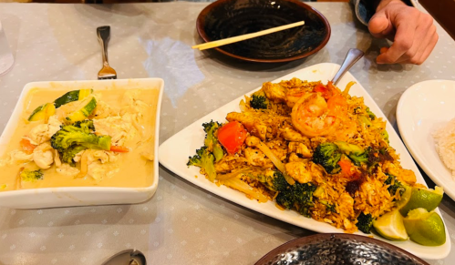 A table with two dishes: one with shrimp and broccoli in a creamy sauce, and another with chicken, shrimp, and rice.