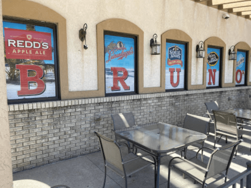 Outdoor seating area with tables in front of a building featuring colorful beer advertisements on the windows.