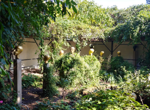 A lush garden with overgrown greenery and several golden head sculptures peeking through the foliage.