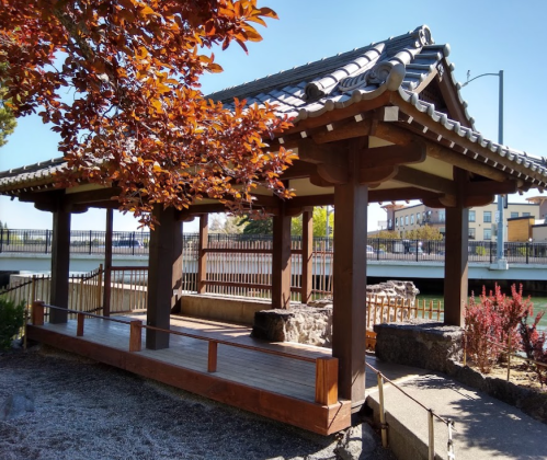 A traditional pavilion with a wooden structure, surrounded by colorful foliage and a serene landscape.