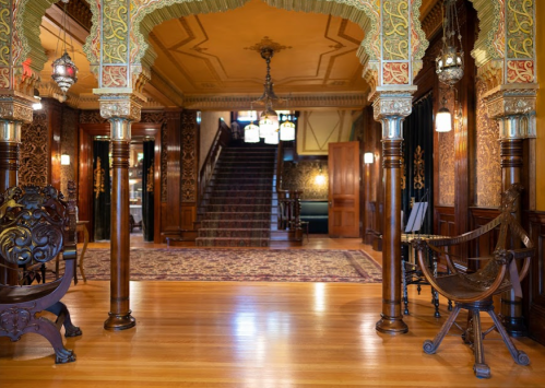 Ornate interior of a historic building featuring intricate woodwork, a staircase, and decorative lighting.