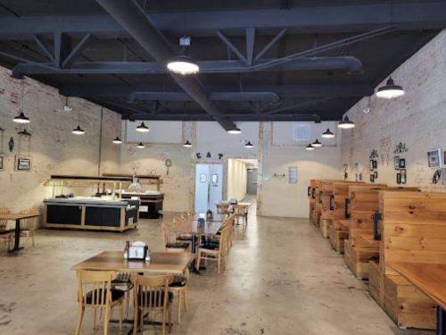 Interior of a spacious restaurant featuring wooden booths, tables, and a serving area with industrial-style lighting.