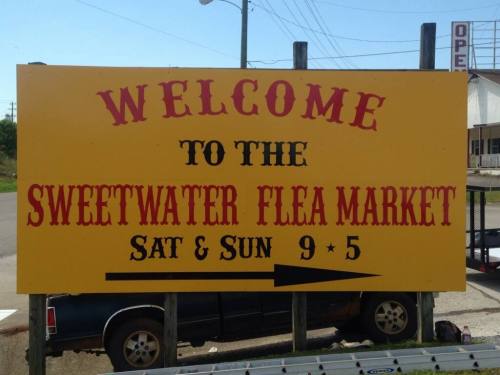 A large yellow sign welcoming visitors to the Sweetwater Flea Market, open Saturday and Sunday from 9 to 5.